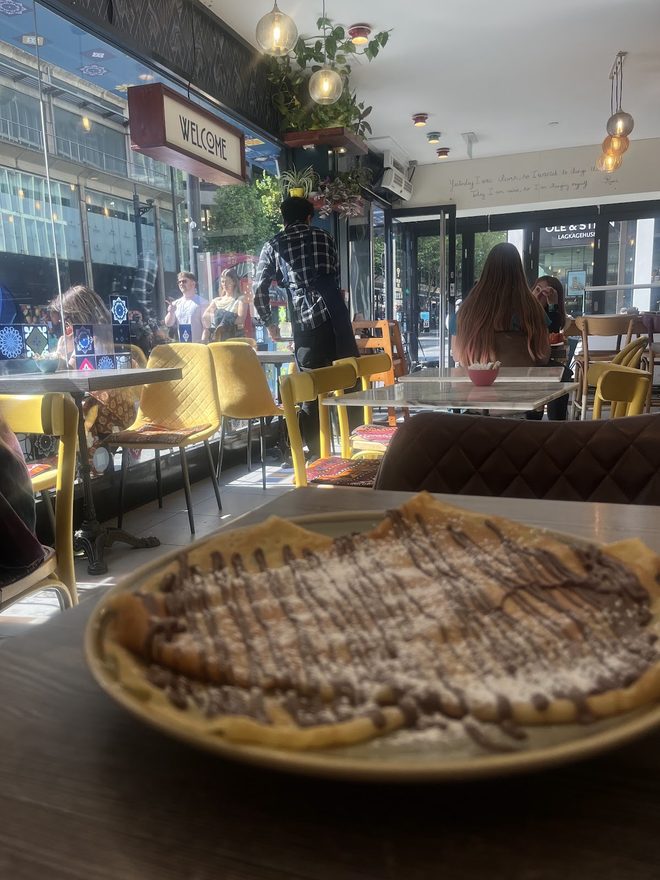 A crêpe on the table with the sunlit café front and the street beyond.