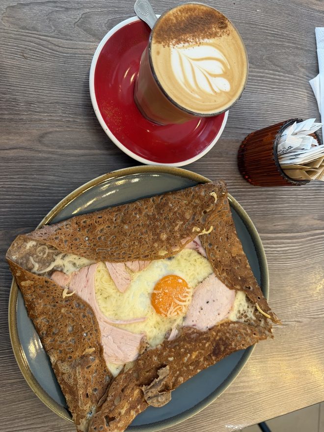 Savoury galette with a fried egg beside a leaf-art latte.