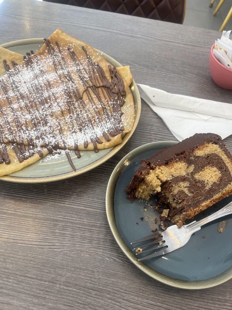 Crêpe with icing sugar and chocolate drizzle, with a slice of marble cake.